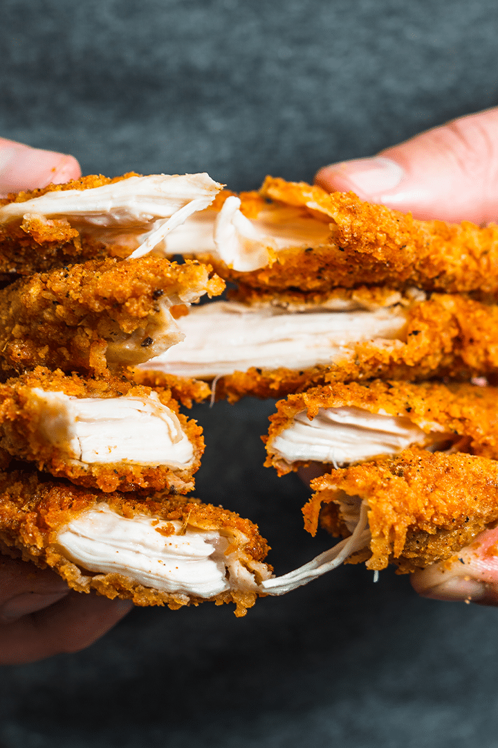 Chicken tenders being pulled apart, revealing juicy white meat inside.